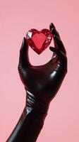 Heart shaped ruby held by a gloved hand against a pink background in artistic display photo