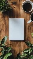 Blank notebook and coffee cups on wooden table surrounded by green plants in a cozy setting photo