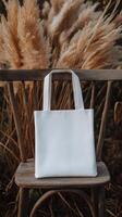 White tote bag placed on a wooden chair amidst dry grass in a tranquil outdoor setting photo