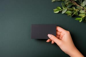 Hand holding a blank black card against a dark green background in a minimalist composition photo