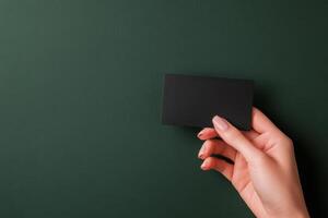 Hand holding a blank black card against a dark green background in a minimalist composition photo