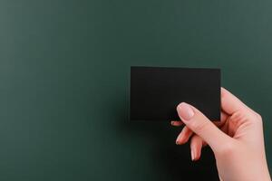 Hand holding a blank black card against a dark green background in a minimalist composition photo