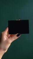Hand holding a black card against a dark green background in a contemporary setting photo