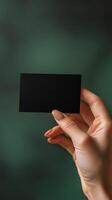 Hand holding a black card against a dark green background in a contemporary setting photo