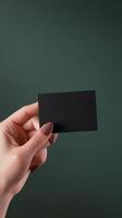 Hand holding a black card against a dark green background in a contemporary setting photo