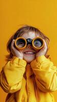 Child with binoculars enjoys playful exploration against a vibrant yellow background photo