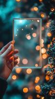 Hand holding a blank transparent frame against a background of glowing Christmas lights photo