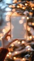 Hand holding a blank transparent frame against a background of glowing Christmas lights photo