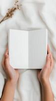Open blank notebook held by hands on soft fabric with dried flowers nearby in natural light photo