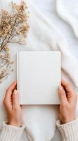 Open blank notebook held by hands on soft fabric with dried flowers nearby in natural light photo