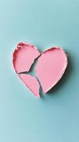 Broken heart shaped object in pastel pink color on light blue surface photo
