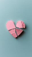 Broken heart shaped object in pastel pink color on light blue surface photo