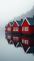 Red wooden cabins reflect on still water in a foggy coastal setting photo