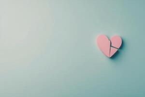 Pink heart shaped piece broken on a light blue background representing love and relationships photo