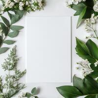 Fresh greenery and delicate flowers surround a blank white sheet on a neutral background photo