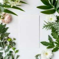 Fresh greenery and delicate flowers surround a blank white sheet on a neutral background photo