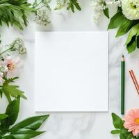 Fresh greenery and delicate flowers surround a blank white sheet on a neutral background photo