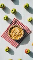 Freshly baked apple pie surrounded by green apples on a checkered cloth photo
