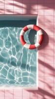 Bright and colorful lifebuoy hanging on pink tiled wall above clear swimming pool water photo