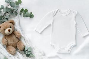 Cute baby outfit and bear arranged on a soft blanket with greenery accents photo
