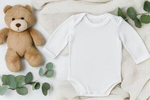Cute baby outfit and bear arranged on a soft blanket with greenery accents photo