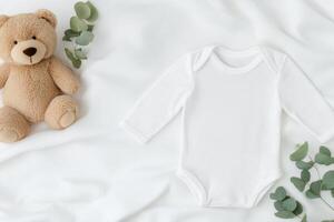 Cute baby outfit and bear arranged on a soft blanket with greenery accents photo