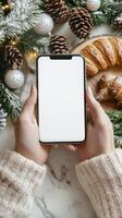 Cozy winter setting with hands holding a smartphone and delicious pastry around festive decorations photo