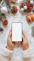 Cozy winter setting with hands holding a smartphone and delicious pastry around festive decorations photo
