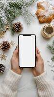 Cozy winter setting with hands holding a smartphone and delicious pastry around festive decorations photo