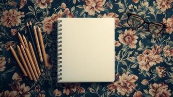 Blank sketchbook and colored pencils on floral patterned tablecloth in a creative workspace photo