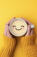 Cozy hands holding warm drink with smiley face on yellow background photo