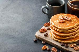 Stack of fluffy pancakes with pecans on a wooden board against a dark background photo