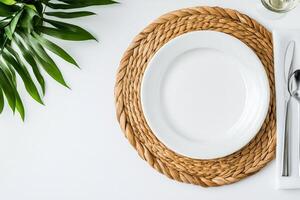 Clean white plate on a woven placemat surrounded by green foliage and cutlery photo
