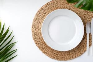 Clean white plate on a woven placemat surrounded by green foliage and cutlery photo
