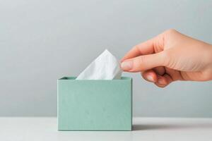 Hand reaching for tissue from a teal box on a white table in a calm environment photo