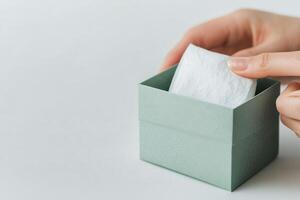 Hand reaching for tissue from a teal box on a white table in a calm environment photo