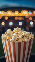 Fresh popcorn in a striped container at a lively outdoor event during twilight hours photo