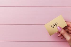 Elegant hand holding a stylish VIP card against a soft pink background photo