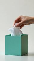 Hand reaching into a green tissue box to pull out a paper tissue for use photo