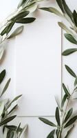 Decorative arrangement of olive leaves framing a blank sheet of textured paper on a light background photo