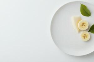 Slices of banana placed on a white plate with fresh green leaves nearby photo