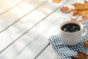 Warm coffee cup resting on a checkered napkin surrounded by autumn leaves photo