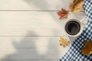 Warm coffee cup resting on a checkered napkin surrounded by autumn leaves photo