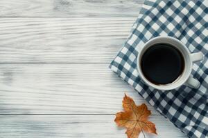 Warm coffee cup resting on a checkered napkin surrounded by autumn leaves photo