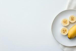 Slices of banana placed on a white plate with fresh green leaves nearby photo