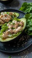 Healthy avocado halves filled with chicken salad on a black plate with greens photo
