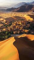 Scenic view of a desert oasis village surrounded by golden sand dunes at sunset photo