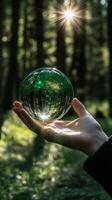 Hand holding a transparent green globe reflecting nature in a forest setting photo