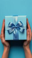 Gift wrapped in light blue with satin bow held by hands against a vibrant background photo