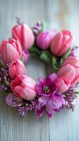 Delicate floral wreath with pink tulips and purple blooms on wooden surface photo